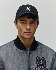 Mens Jimmy Baseball Cap in black with a white embroidered Psycho Bunny skull logo, paired with a black and white herringbone bomber jacket featuring a large embroidered Psycho Bunny skull patch.