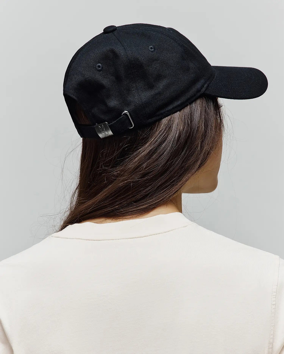 Black Mens Jimmy Baseball Cap in smooth twill, featuring a silver adjustable buckle with a small engraved Psycho Bunny skull logo, paired with a cream classic fit jersey t-shirt.