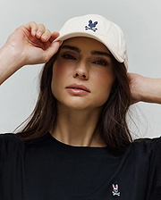 Cream Mens Jimmy Baseball Cap with an embroidered navy Psycho Bunny skull logo, paired with a black classic fit jersey t-shirt featuring a small embroidered pink and white Psycho Bunny skull logo on the left chest.