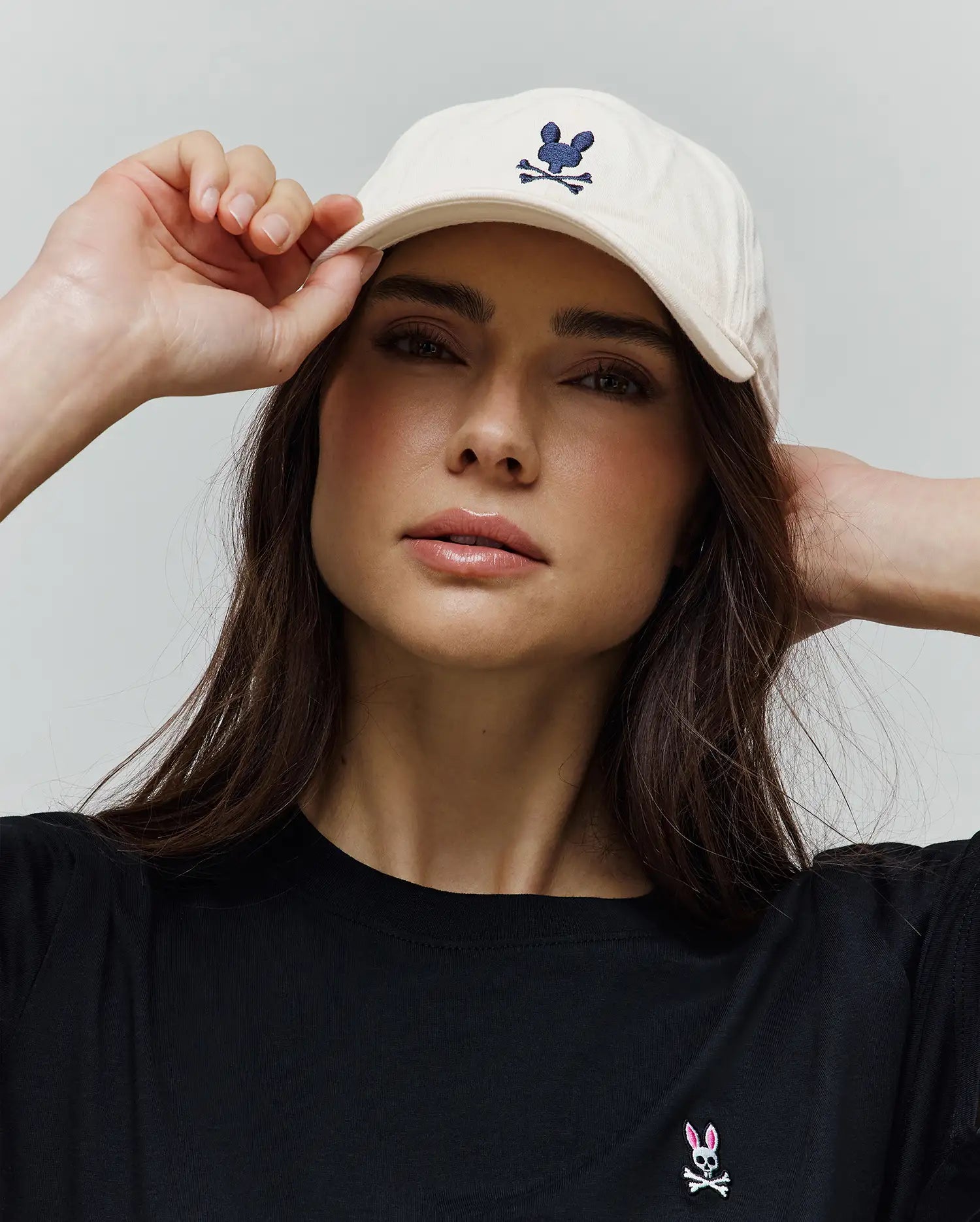 Cream Mens Jimmy Baseball Cap with an embroidered navy Psycho Bunny skull logo, paired with a black classic fit jersey t-shirt featuring a small embroidered pink and white Psycho Bunny skull logo on the left chest.