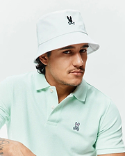 Light mint green pique polo shirt with a small embroidered Psycho Bunny logo on the chest, paired with a white Mens Jimmy Bucket Hat featuring a black embroidered bunny skull.