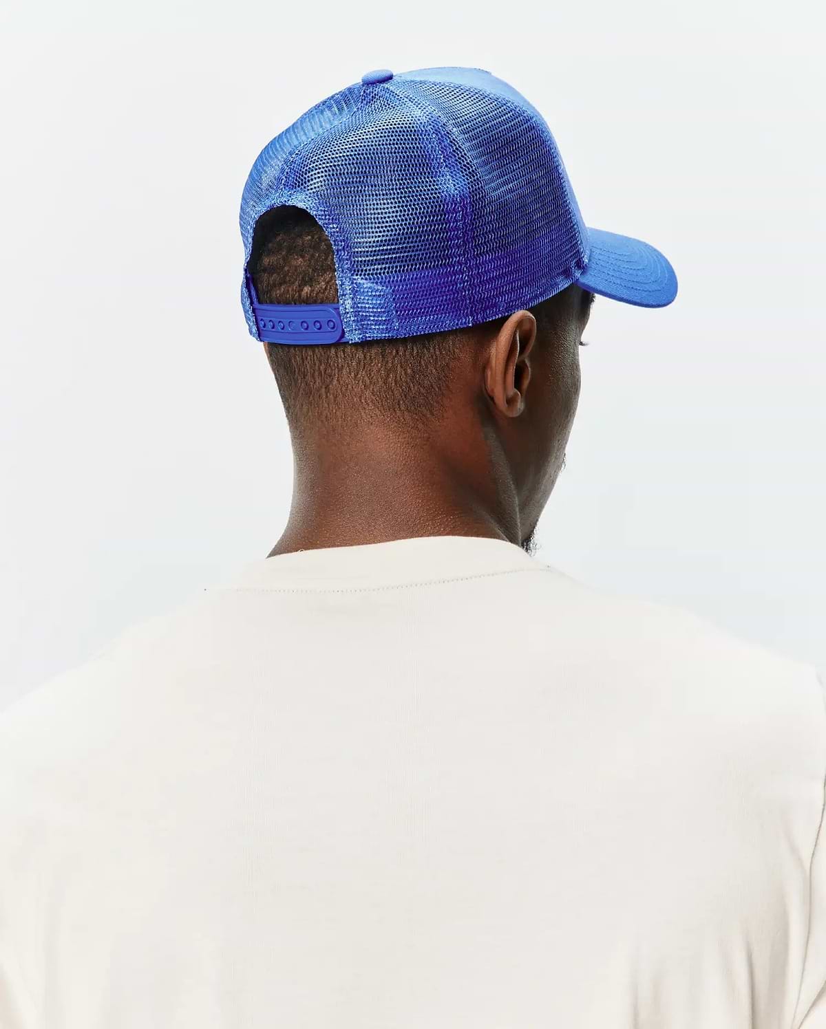 Mens Tobias Trucker Cap in vibrant royal blue, featuring a mesh back, solid front panel, curved brim, and adjustable snap closure, worn with a cream classic fit jersey knit t-shirt.