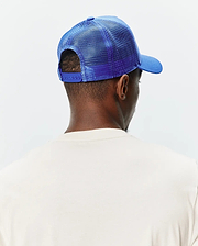 Mens Tobias Trucker Cap in vibrant royal blue, featuring a mesh back, solid front panel, curved brim, and adjustable snap closure, worn with a cream classic fit jersey knit t-shirt.
