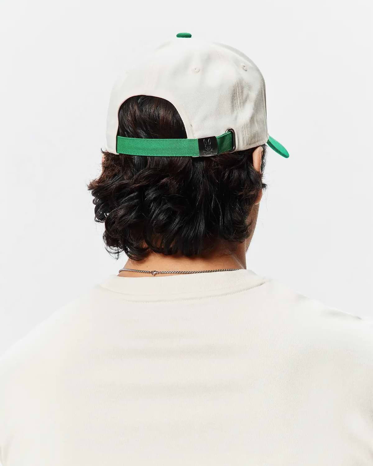 Mens Craig Baseball Cap in cream cotton twill with a green brim and adjustable strap featuring a small Psycho Bunny skull logo on the metal buckle.