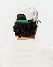 Mens Craig Baseball Cap in cream cotton twill with a green brim and adjustable strap featuring a small Psycho Bunny skull logo on the metal buckle.