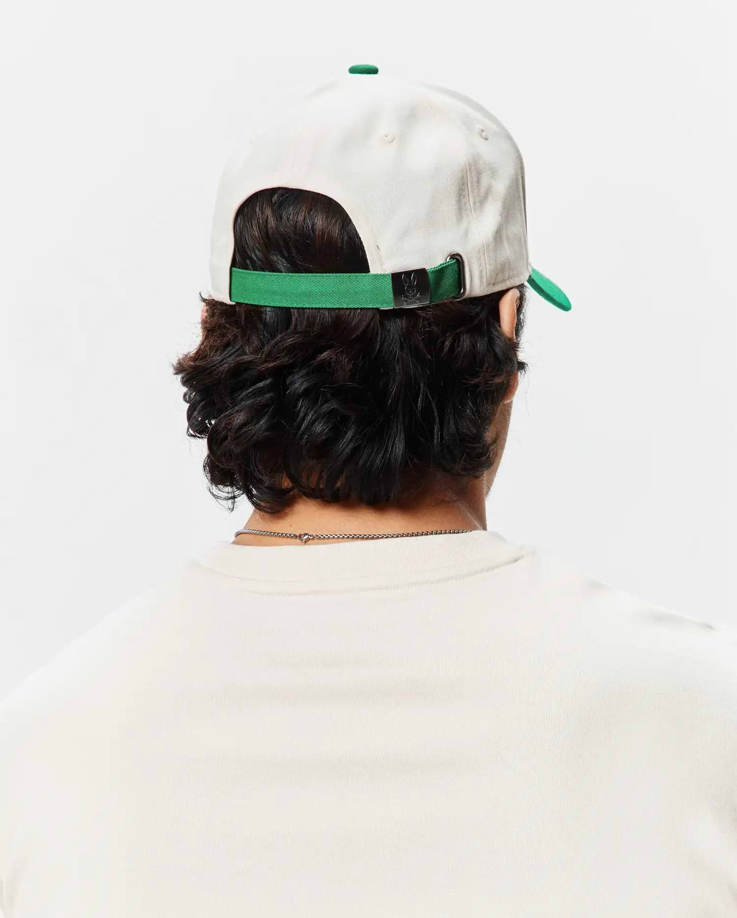 Mens Craig Baseball Cap in cream cotton twill with a green brim and adjustable strap featuring a small Psycho Bunny skull logo on the metal buckle.