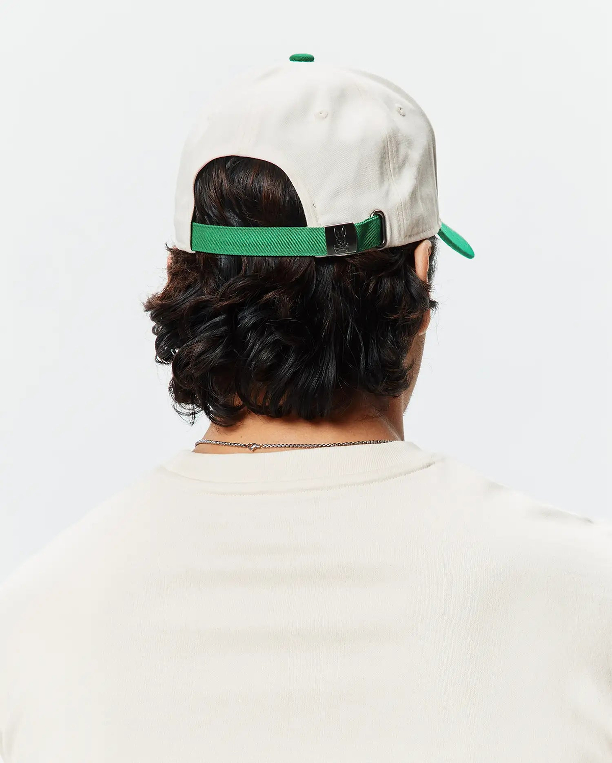 Mens Craig Baseball Cap in cream cotton twill with a green brim and adjustable strap featuring a small Psycho Bunny skull logo on the metal buckle.