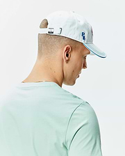 White cotton twill Mens Ray Baseball Cap with blue embroidered PB initials, blue brim stitching, and a metal Psycho Bunny skull buckle, paired with a mint green jersey knit crew neck t-shirt.