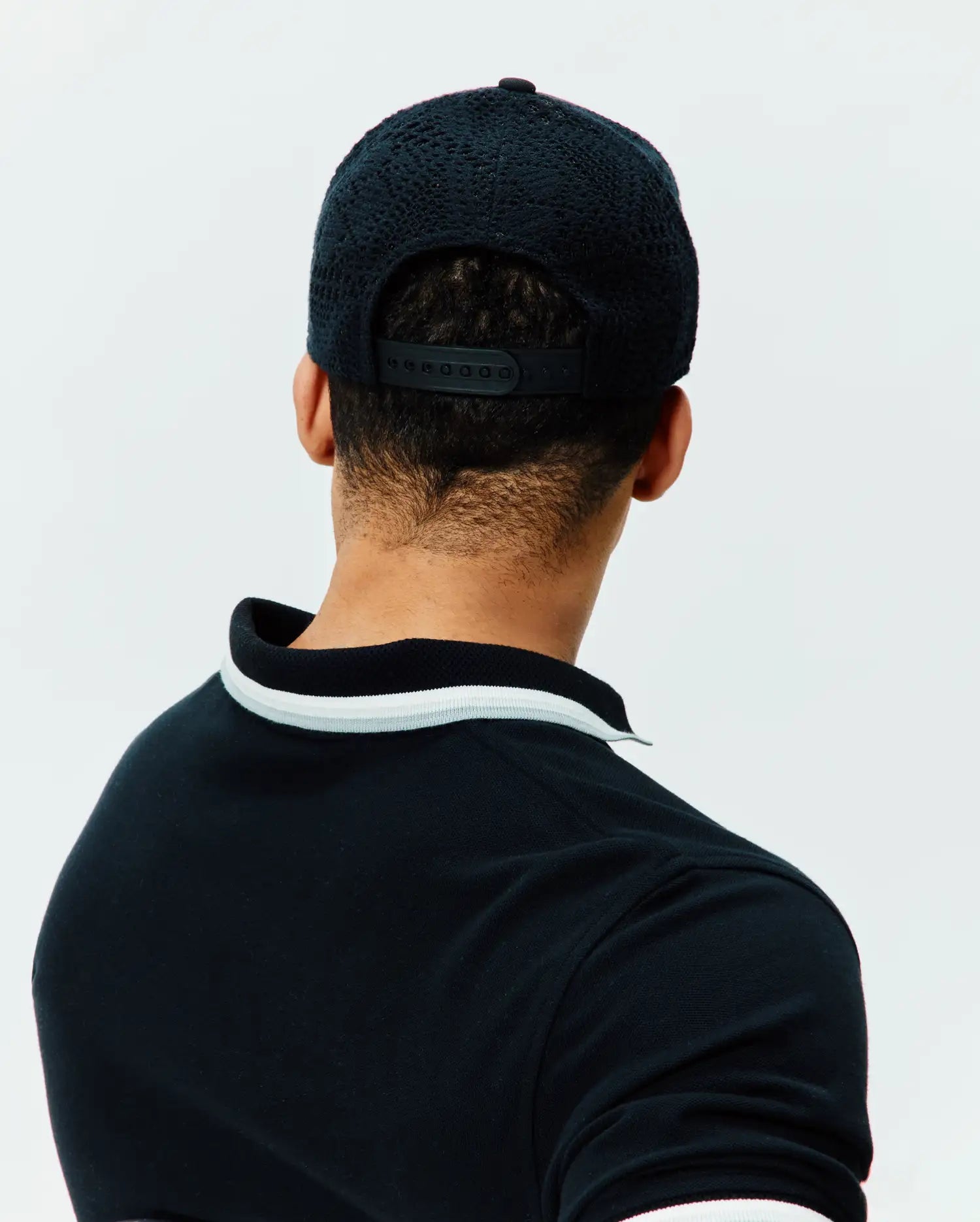 Black pique polo shirt with ribbed collar and cuffs, accented by white stripes, paired with a black mesh-back Mens Elijah Trucker Cap featuring a snapback closure.
