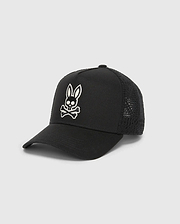 Mens Elijah Trucker Cap, a black premium streetwear cap featuring a prominent white embroidered Psycho Bunny skull logo on the front, with a solid cotton twill front panel and breathable mesh back.