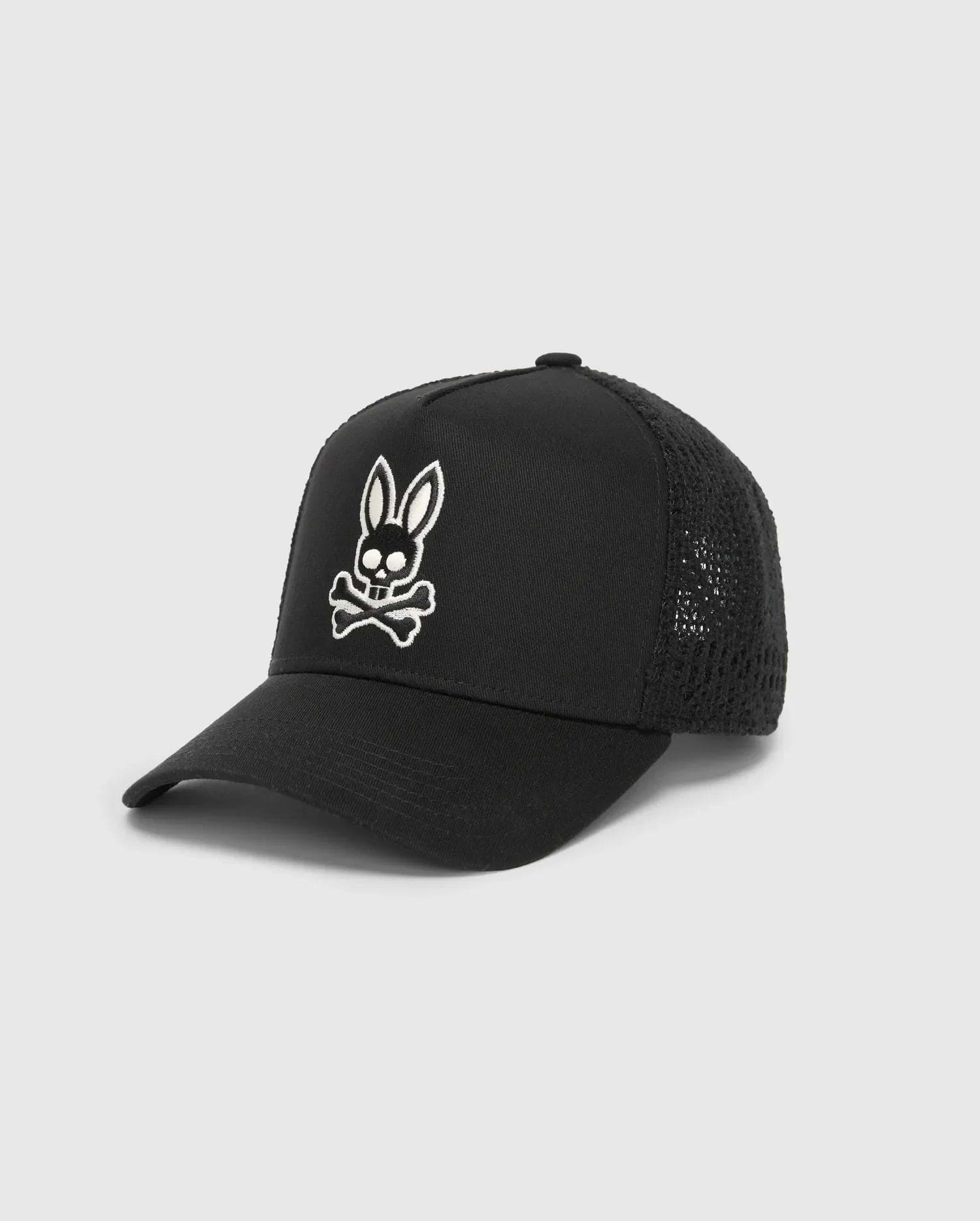Mens Elijah Trucker Cap, a black premium streetwear cap featuring a prominent white embroidered Psycho Bunny skull logo on the front, with a solid cotton twill front panel and breathable mesh back.