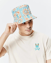 Mens Frank Reversible Bucket Hat in white with blue and orange mandala-style patterns featuring repeated Psycho Bunny skull logos, paired with a cream jersey t-shirt displaying a large blue and orange Psycho Bunny skull logo on the left chest.