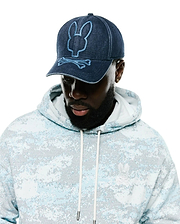 Men's Grover Baseball Cap in dark denim with light blue embroidered Psycho Bunny logo, paired with a relaxed fit french terry hoodie featuring a light blue digital camo print and a small white embroidered Psycho Bunny chest logo. (1)