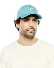 Men's Alfie Baseball Cap in aqua cotton twill with an embroidered Psycho Bunny skull logo on the front, paired with a cream jersey t-shirt featuring a subtle embossed Psycho Bunny text on the chest. (1)