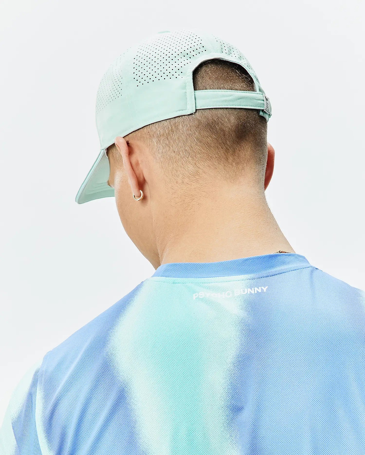 Mens Blaze Sport Cap in mint green with perforated panels and a blue and aqua tie-dye mesh t-shirt featuring a small white Psycho Bunny text logo on the back. (3)