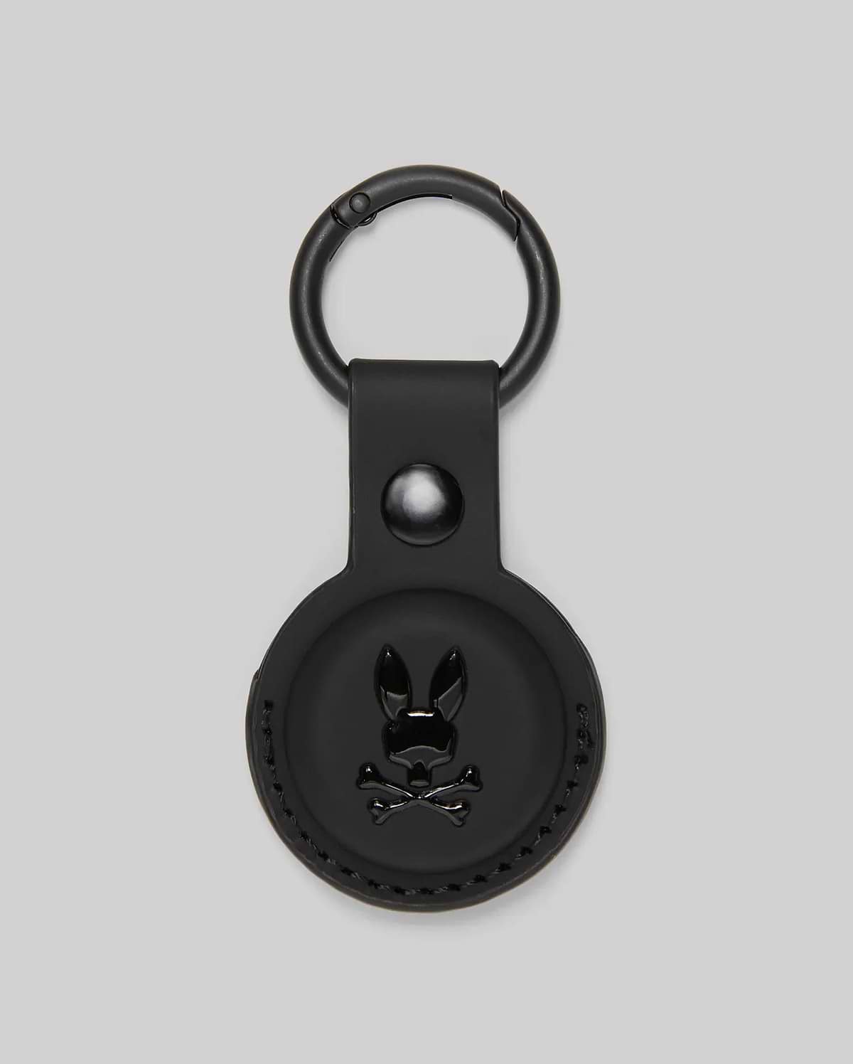 The Psycho Bunny MENS AIR TAG HOLDER - MO1700017 features black leather, a circular design, embossed Bunny logo with crossbones on the front, and a metal keyring—ideal for stylishly securing your keys or luggage tag.