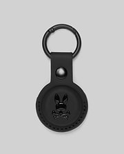 The Psycho Bunny MENS AIR TAG HOLDER - MO1700017 features black leather, a circular design, embossed Bunny logo with crossbones on the front, and a metal keyring—ideal for stylishly securing your keys or luggage tag.