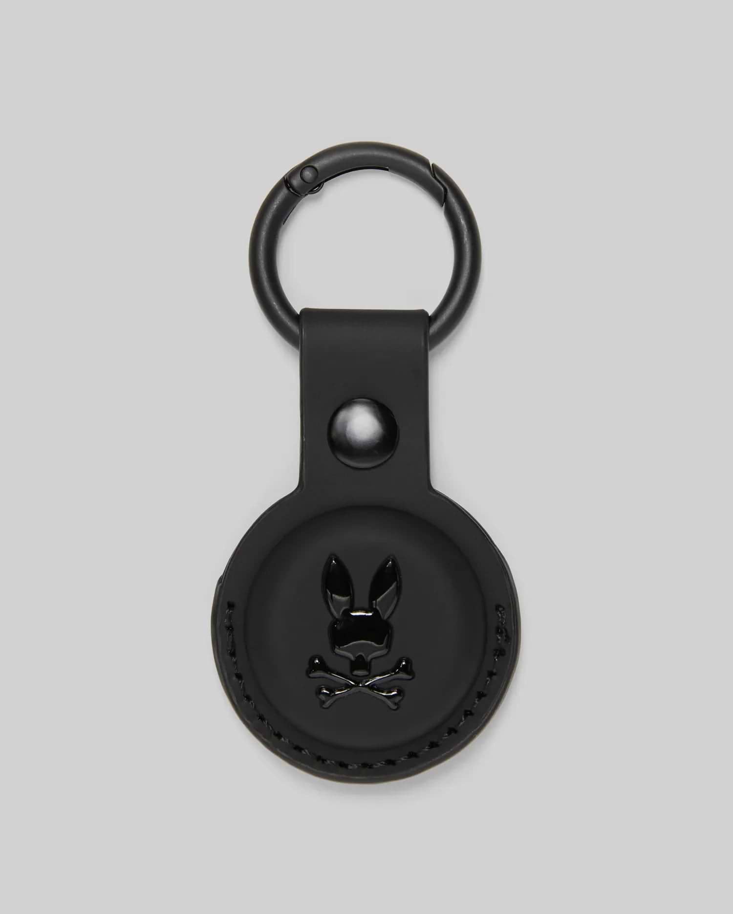 The Psycho Bunny MENS AIR TAG HOLDER - MO1700017 features black leather, a circular design, embossed Bunny logo with crossbones on the front, and a metal keyring—ideal for stylishly securing your keys or luggage tag.