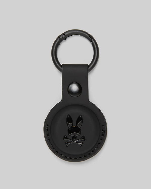 The Psycho Bunny MENS AIR TAG HOLDER - MO1700017 features black leather, a circular design, embossed Bunny logo with crossbones on the front, and a metal keyring—ideal for stylishly securing your keys or luggage tag.