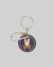 Disc Bunny Keychain featuring a navy blue rubber disc with an orange Psycho Bunny skull logo cutout and orange Psycho Bunny text, attached to a silver metal keyring and carabiner clip. (1)