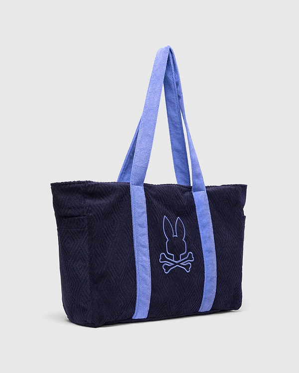 Tristan Towel Tote in navy blue terry cloth with a quilted diamond pattern, featuring light blue straps and a large, centered embroidered Psycho Bunny skull logo.