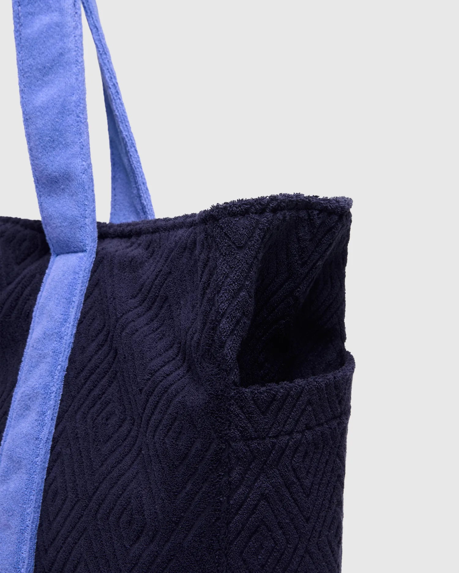 Premium navy terry cloth Tristan Towel Tote, showcasing a textured geometric diamond pattern, with soft periwinkle blue straps and a convenient side pocket.