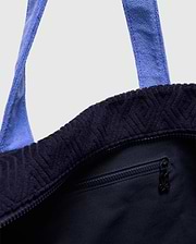 Tristan Towel Tote in deep navy terry cloth, featuring an embossed geometric pattern, light blue towel straps, a top zipper closure, and a small Psycho Bunny skull logo on the zipper pull.