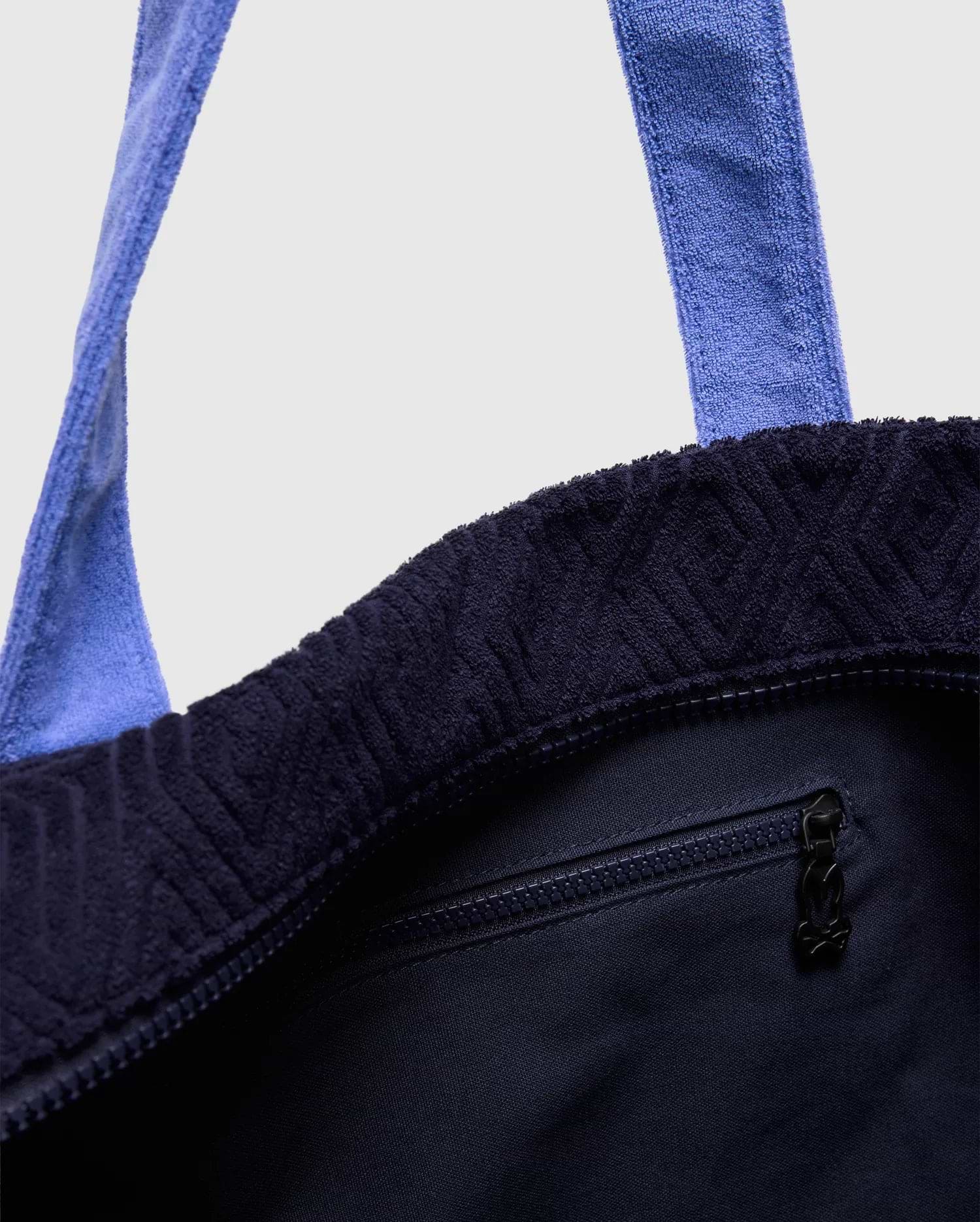 Tristan Towel Tote in deep navy terry cloth, featuring an embossed geometric pattern, light blue towel straps, a top zipper closure, and a small Psycho Bunny skull logo on the zipper pull.