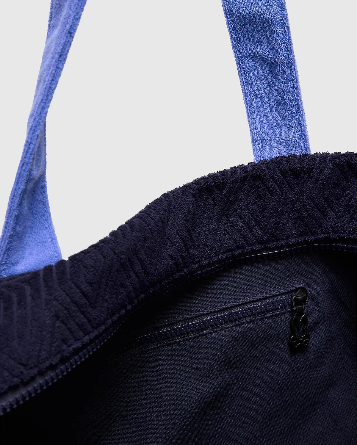 Tristan Towel Tote in deep navy terry cloth, featuring an embossed geometric pattern, light blue towel straps, a top zipper closure, and a small Psycho Bunny skull logo on the zipper pull.