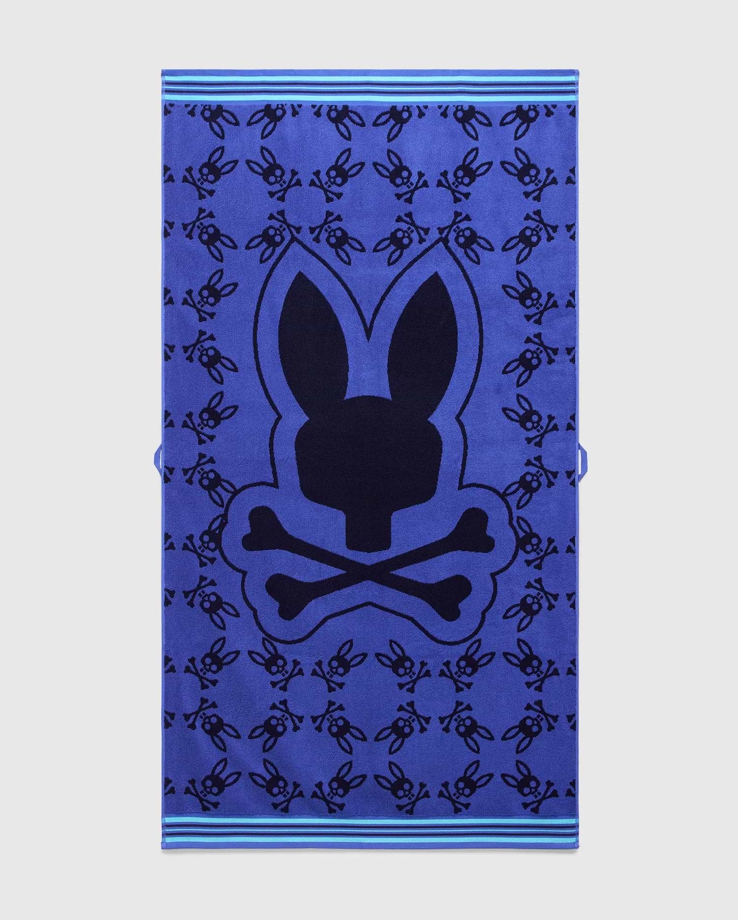 Vibrant blue All Over Bunny Towel featuring a large central dark blue Psycho Bunny skull logo, an all-over pattern of smaller dark blue bunny skulls, and light blue striped borders. (1)