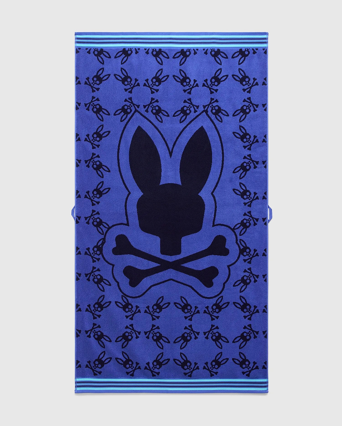 Vibrant blue All Over Bunny Towel featuring a large central dark blue Psycho Bunny skull logo, an all-over pattern of smaller dark blue bunny skulls, and light blue striped borders. (1)