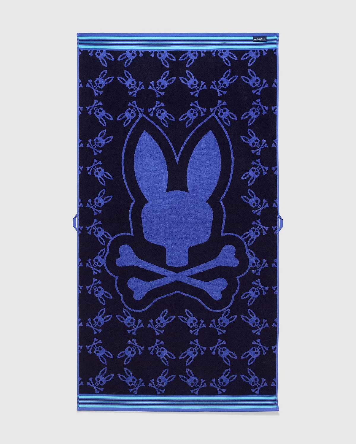 All Over Bunny Towel in navy terry cloth, featuring a large central royal blue bunny skull logo and an all-over smaller bunny skull pattern, with light blue striped borders. (2)
