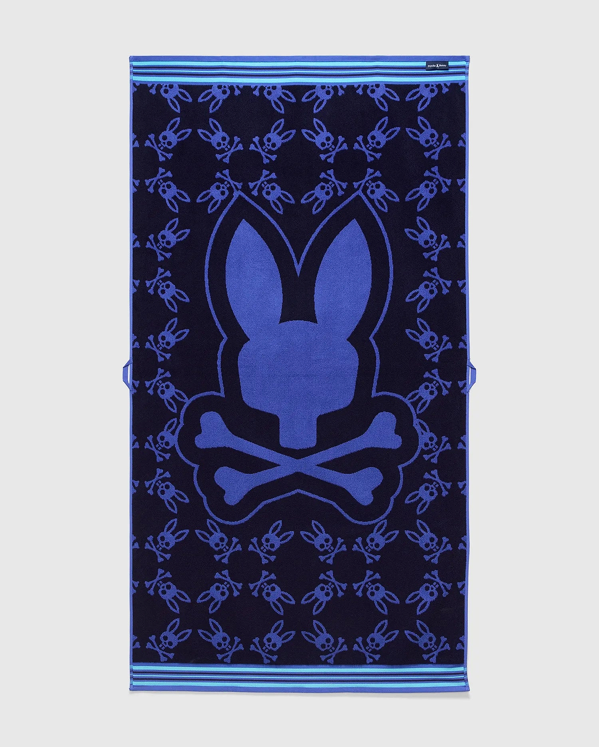 All Over Bunny Towel in navy terry cloth, featuring a large central royal blue bunny skull logo and an all-over smaller bunny skull pattern, with light blue striped borders. (2)