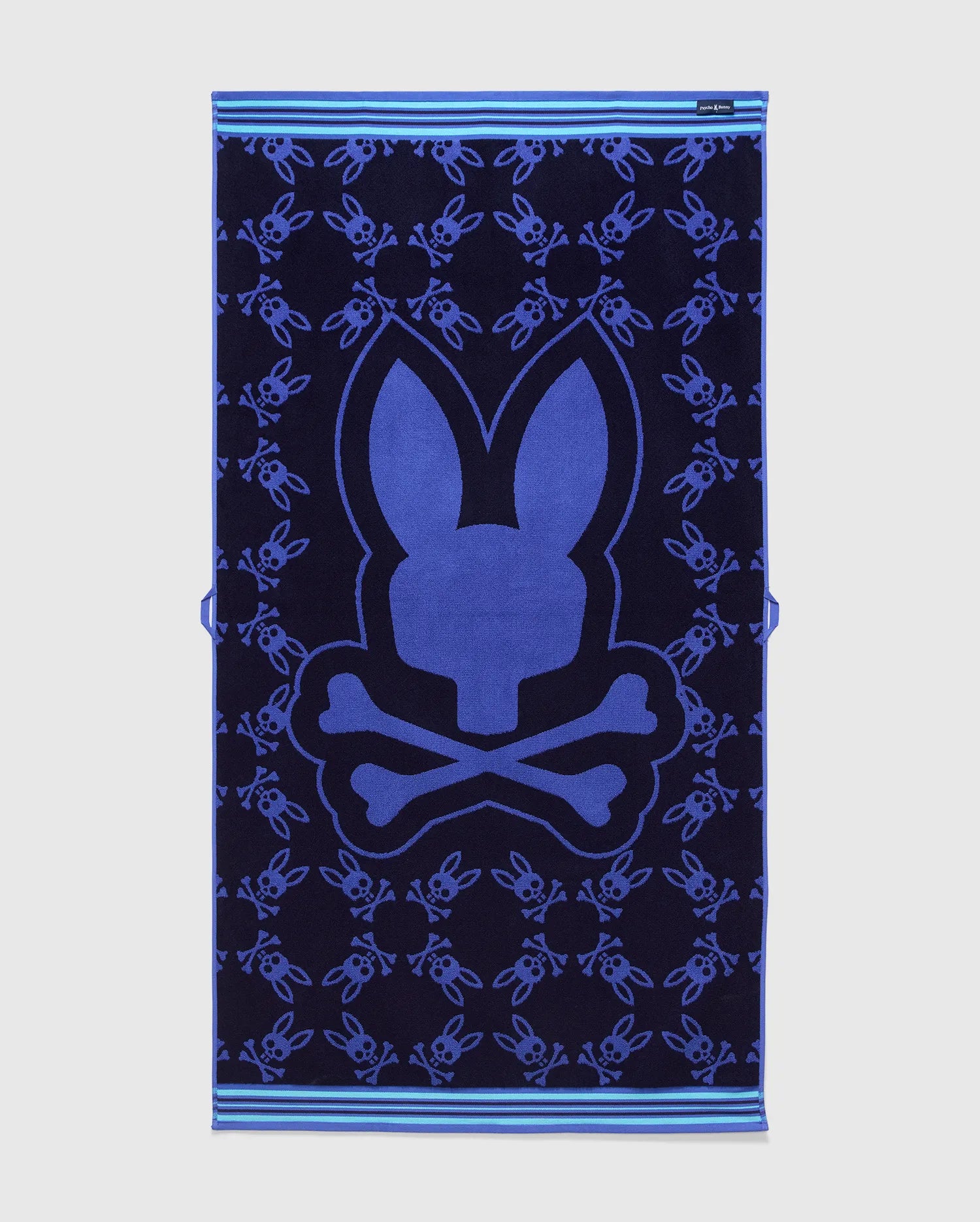 All Over Bunny Towel in navy terry cloth, featuring a large central royal blue bunny skull logo and an all-over smaller bunny skull pattern, with light blue striped borders. (2)