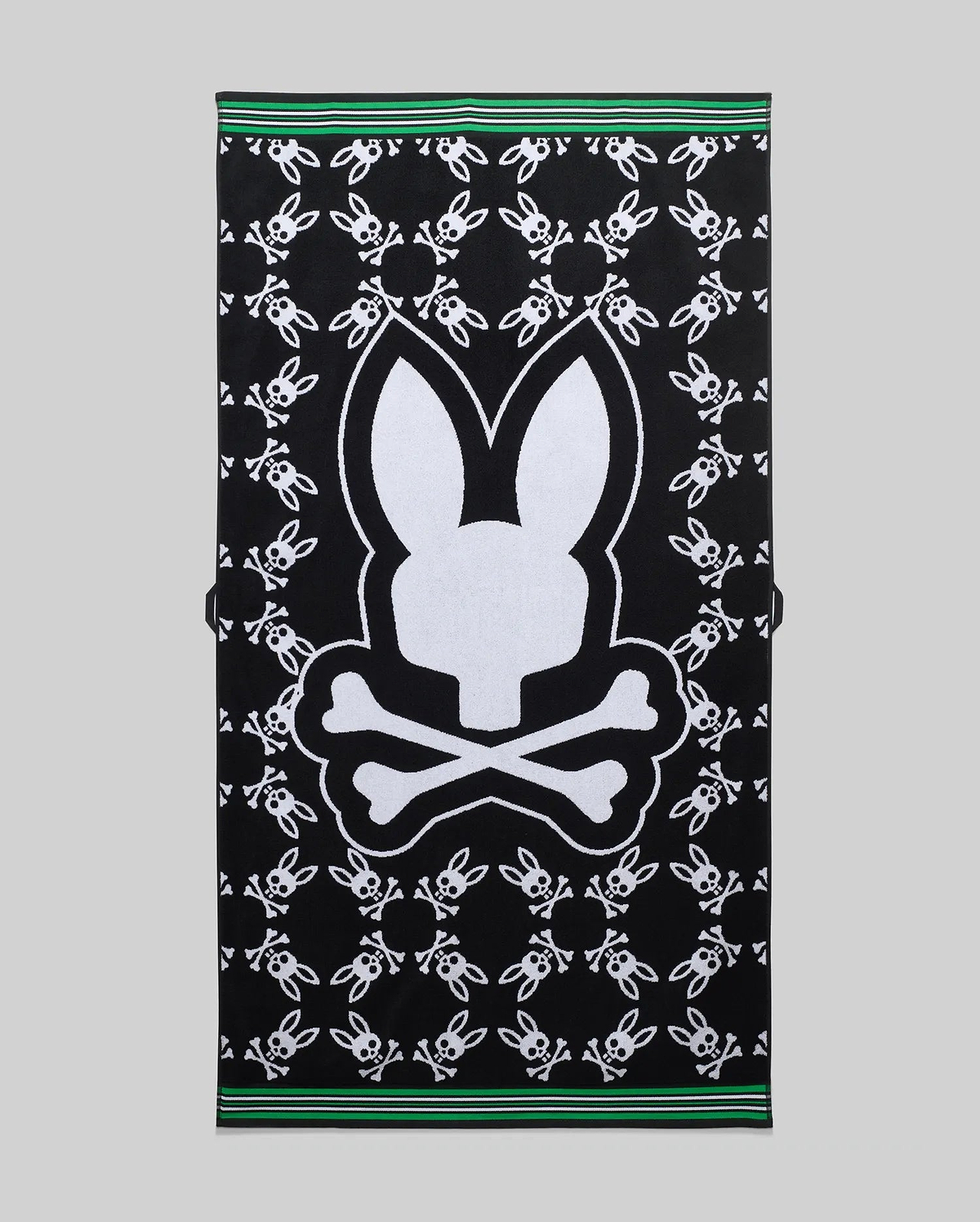 Mens All Over Bunny Towel, black terry cloth featuring a large central white Psycho Bunny skull logo surrounded by smaller white bunny skull logos, with green and white striped borders. (1)