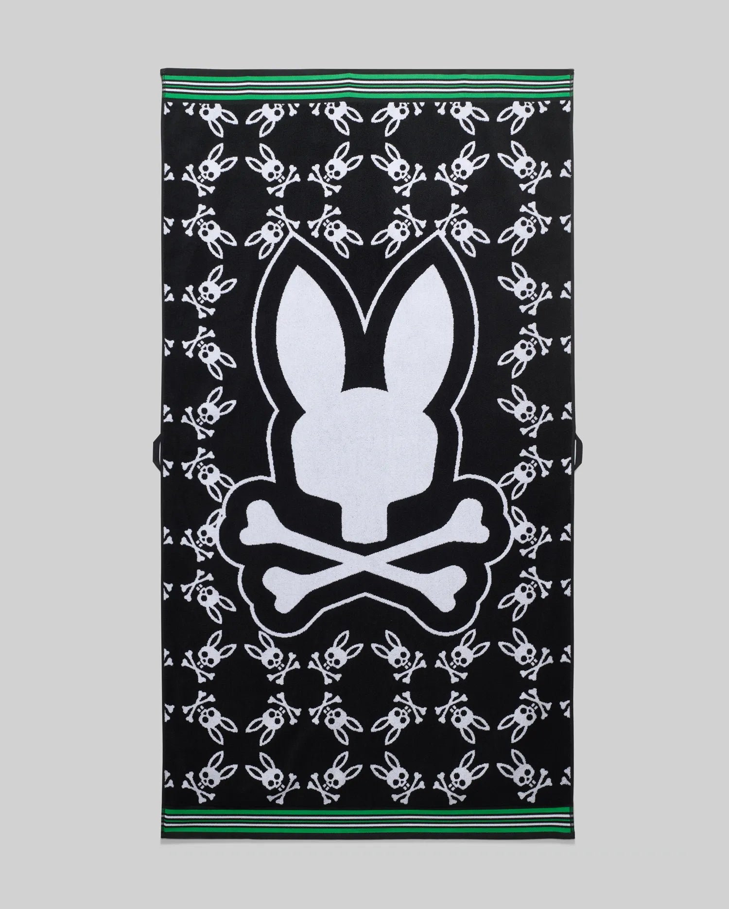 Mens All Over Bunny Towel, black terry cloth featuring a large central white Psycho Bunny skull logo surrounded by smaller white bunny skull logos, with green and white striped borders. (1)