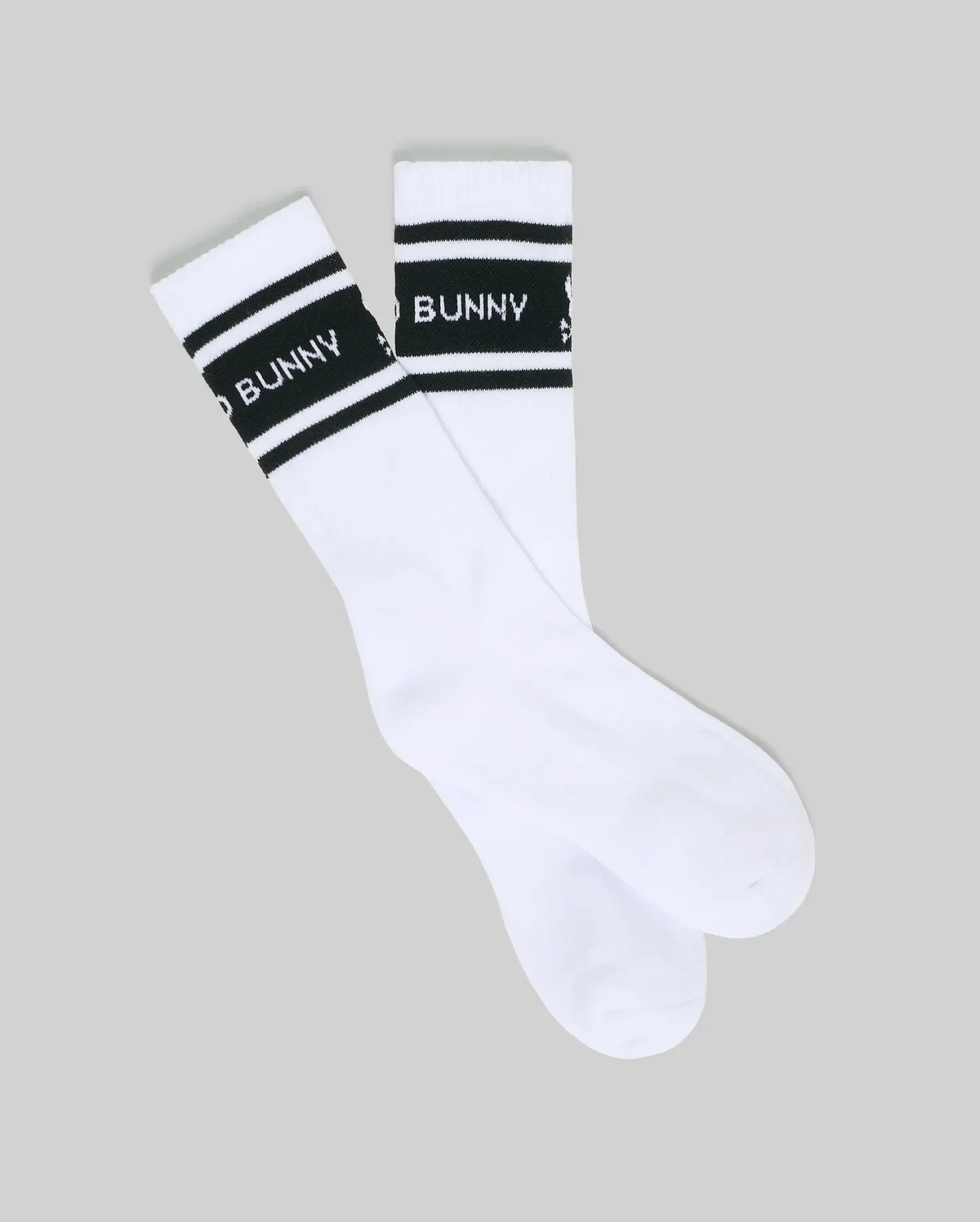 The Psycho Bunny MENS 2 PACK SPORT SOCK - MO2200037 features white cotton sport socks with two black stripes near the top and "BAD BUNNY" text in white on the stripe, laid flat on a light gray background.