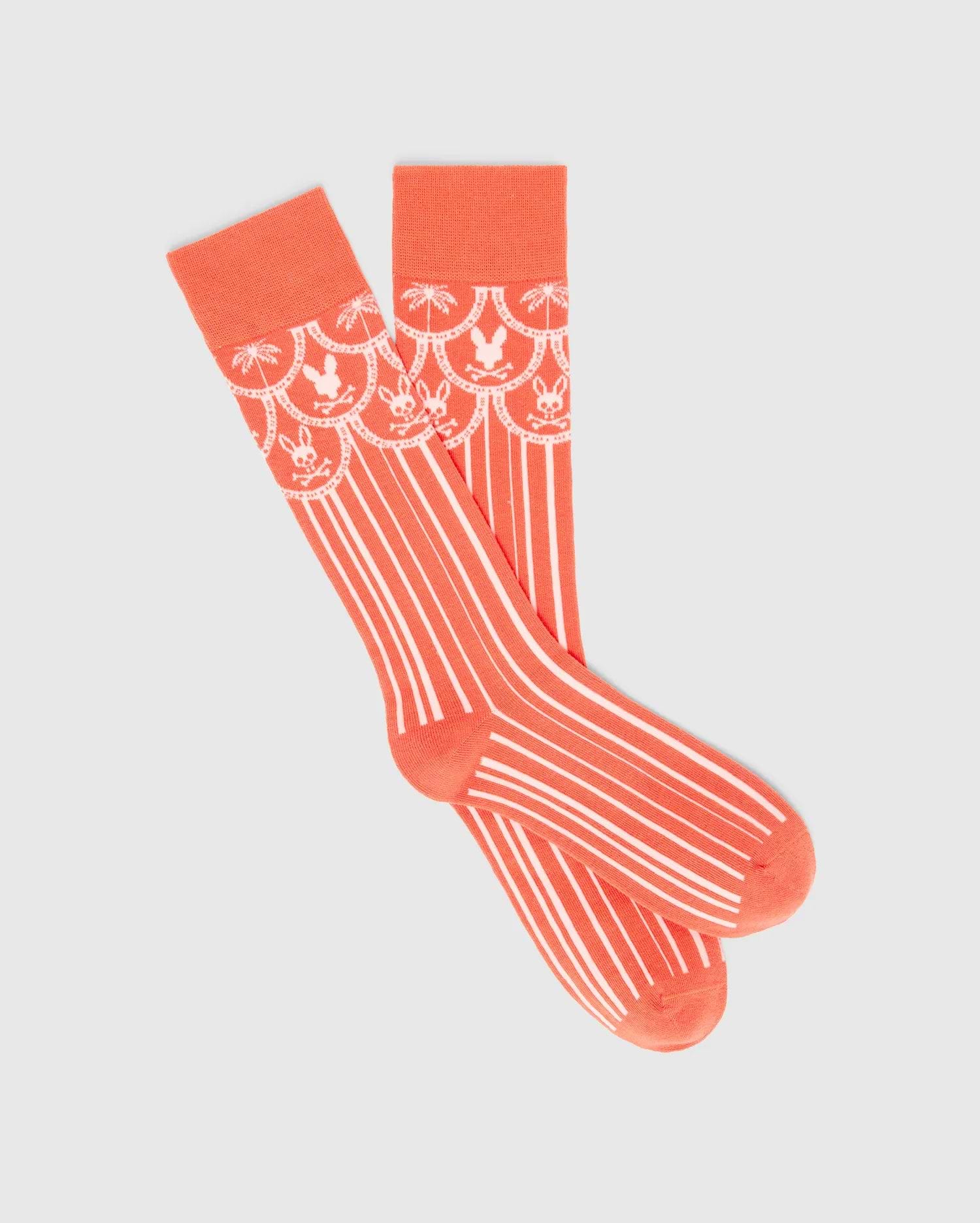 Mens Brad Dress Sock in vibrant coral knit, featuring a white scalloped pattern with alternating Psycho Bunny skull logos and palm trees on the cuff, transitioning to vertical white stripes.