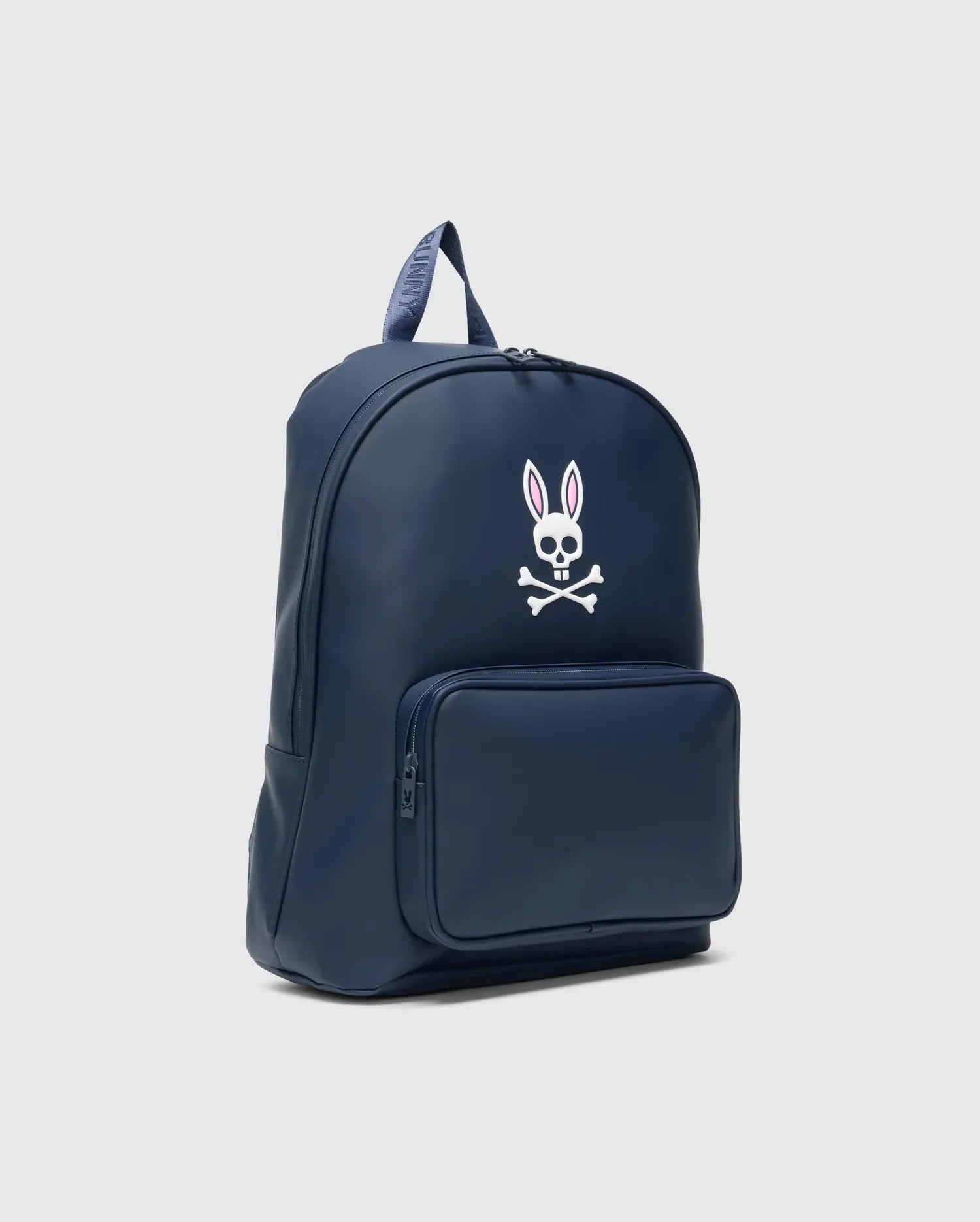 Classic Bunny Backpack in navy blue, featuring a large white and pink Psycho Bunny skull logo on the front, a zippered pocket, and a branded top handle. Smooth finish.