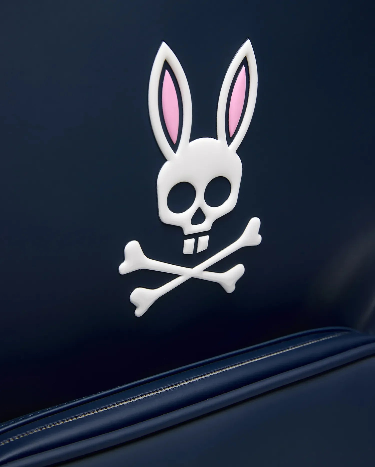 Classic Bunny Backpack in dark navy blue, featuring a large, prominent raised white and pink Psycho Bunny skull and crossbones logo, with a smooth texture and visible zipper detail.