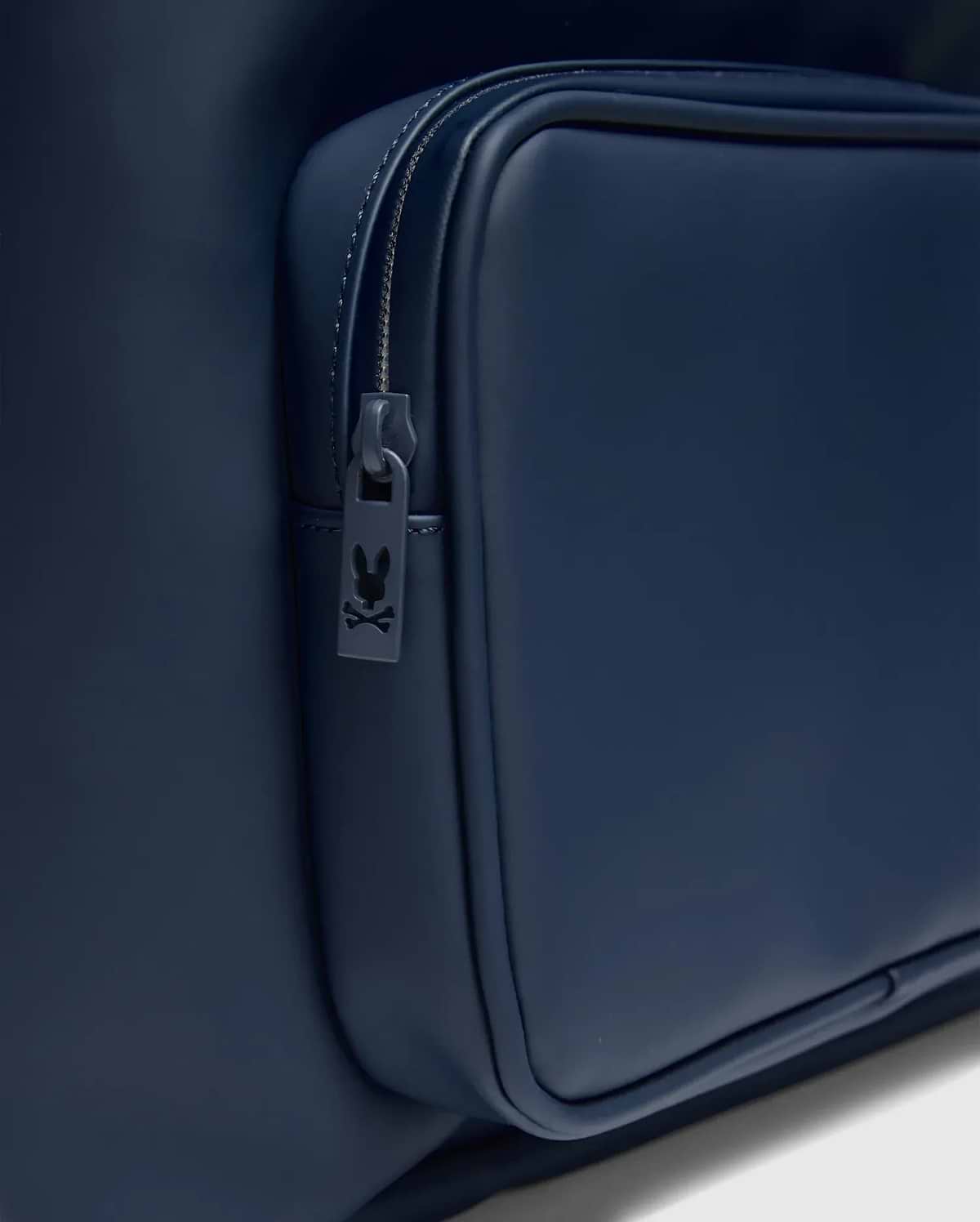 Classic Bunny Backpack in deep navy blue, featuring a smooth matte texture and a zippered front pocket with a small Psycho Bunny logo on the zipper pull.