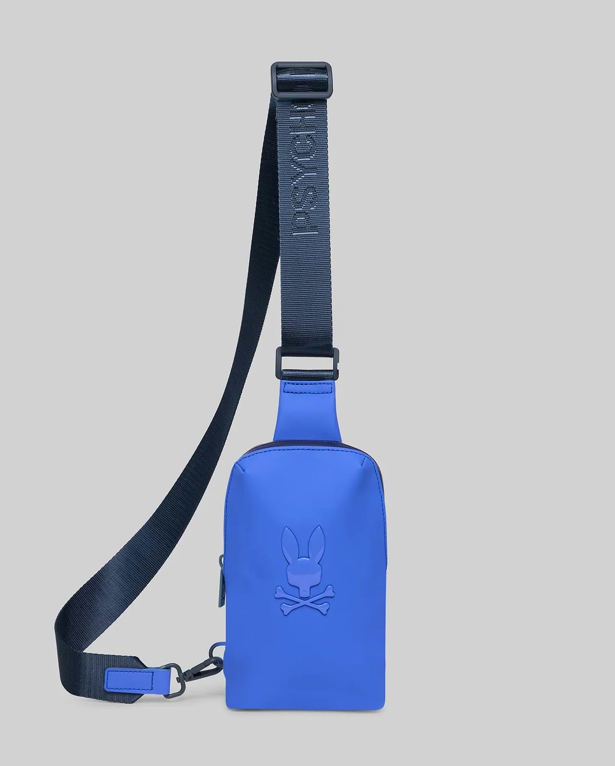 Vibrant blue Rubberized Crossbody Bag featuring a large, tonal embossed Psycho Bunny skull logo on the front. Includes a dark navy adjustable strap with debossed Psycho Bunny branding.