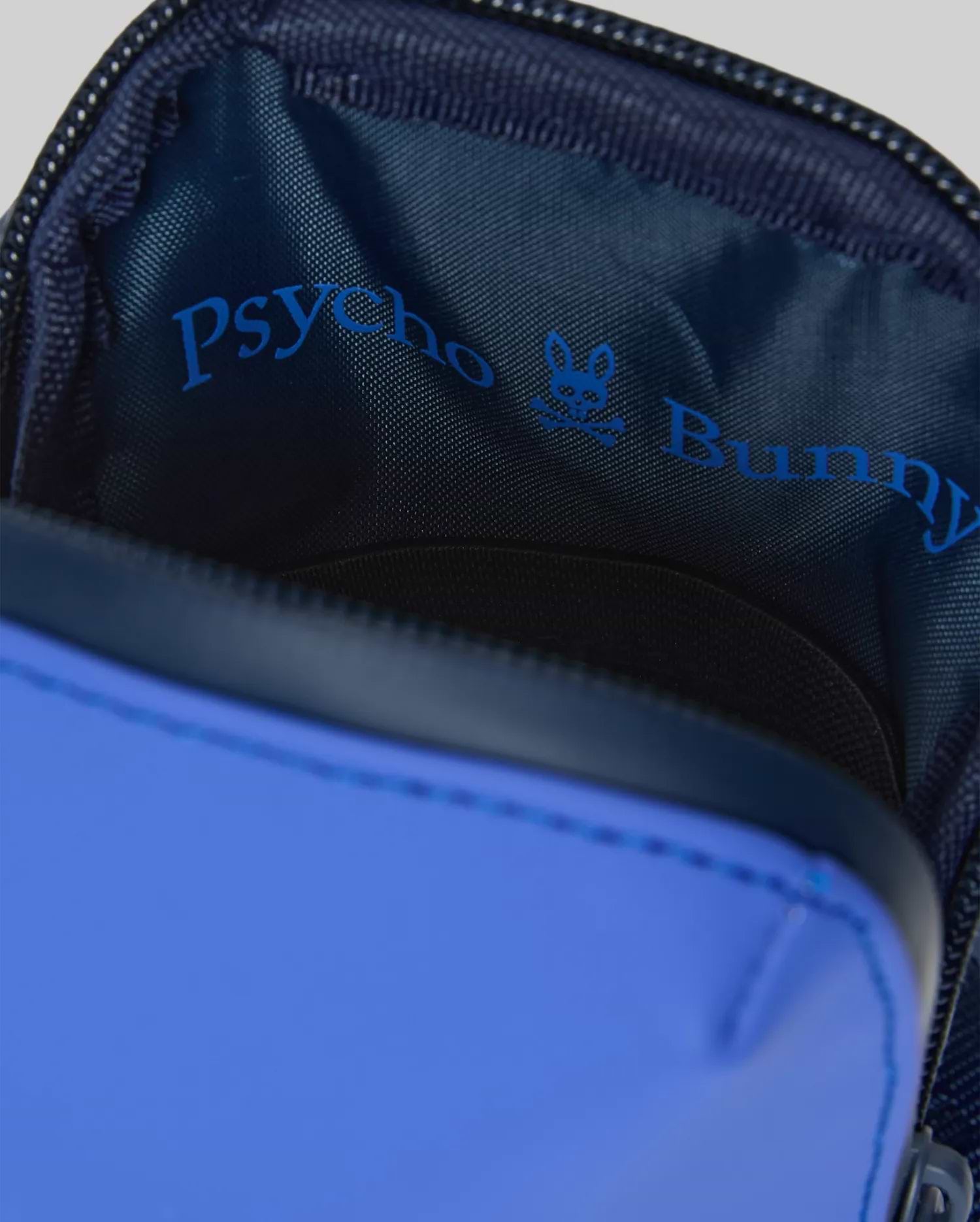 Rubberized Crossbody Bag in royal blue with a smooth exterior, revealing a dark navy woven interior lining featuring a prominent bright blue Psycho Bunny text logo and skull graphic.