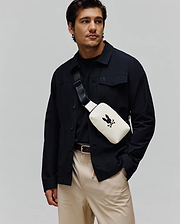 Mens Rubberized Crossbody in off-white, featuring a prominent black Psycho Bunny skull logo on the front and a branded black strap. Smooth texture, sleek design.