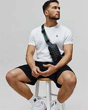 White classic fit jersey t-shirt with embroidered Psycho Bunny skull logo, black textured shorts, and a black Mens Rubberized Crossbody bag with allover skull print and green stripe strap. (4)