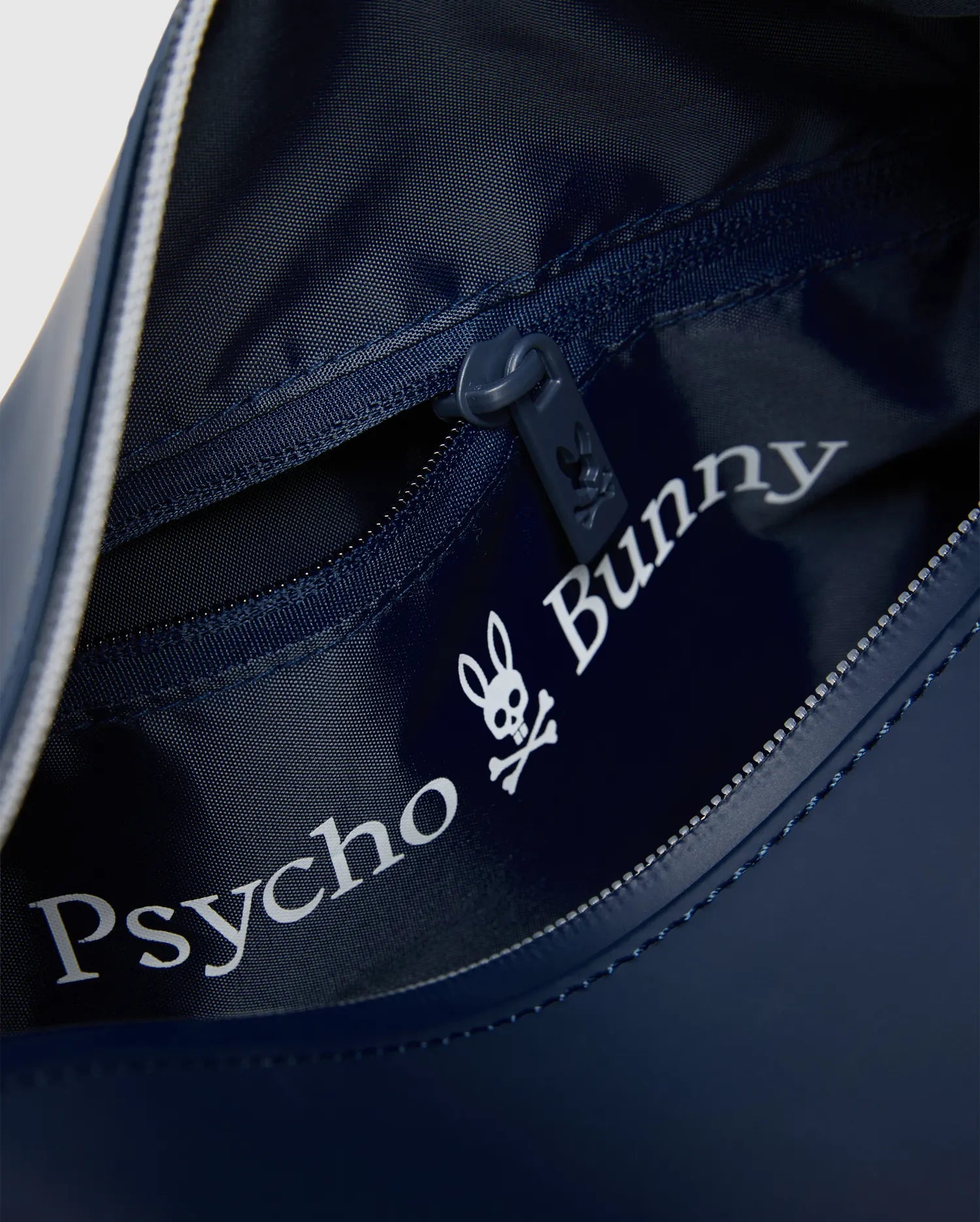 Classic Bunny Toiletry Kit in navy blue, with textured interior lining, zippered main compartment, and large white Psycho Bunny skull logo print inside, plus a small bunny skull on the zipper pull.