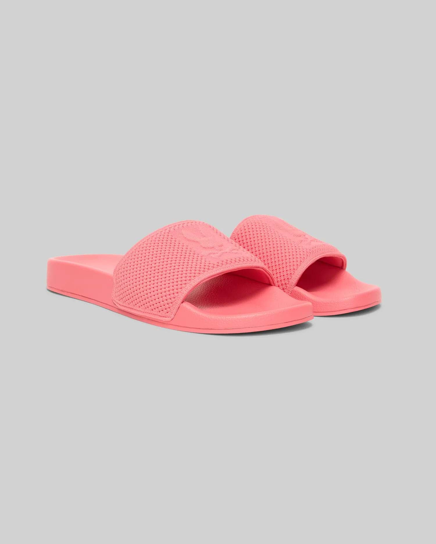 Mens Knit Slides in vibrant coral pink, featuring a textured perforated knit strap with a prominent debossed Psycho Bunny skull logo, and a smooth, monochromatic sole. (1)