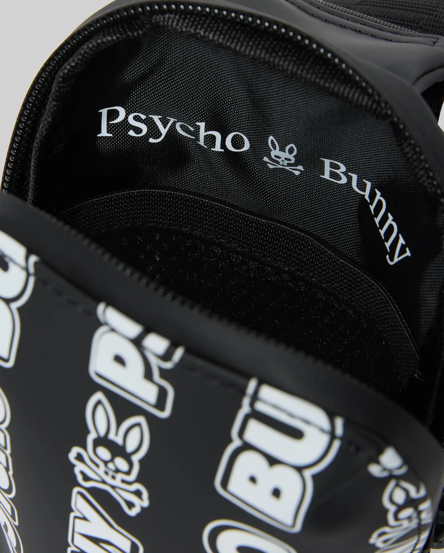 Mens Rubberized Crossbody in black with a white all-over Psycho Bunny text and skull logo print, featuring a rubberized exterior and woven interior lining with repeating branding.