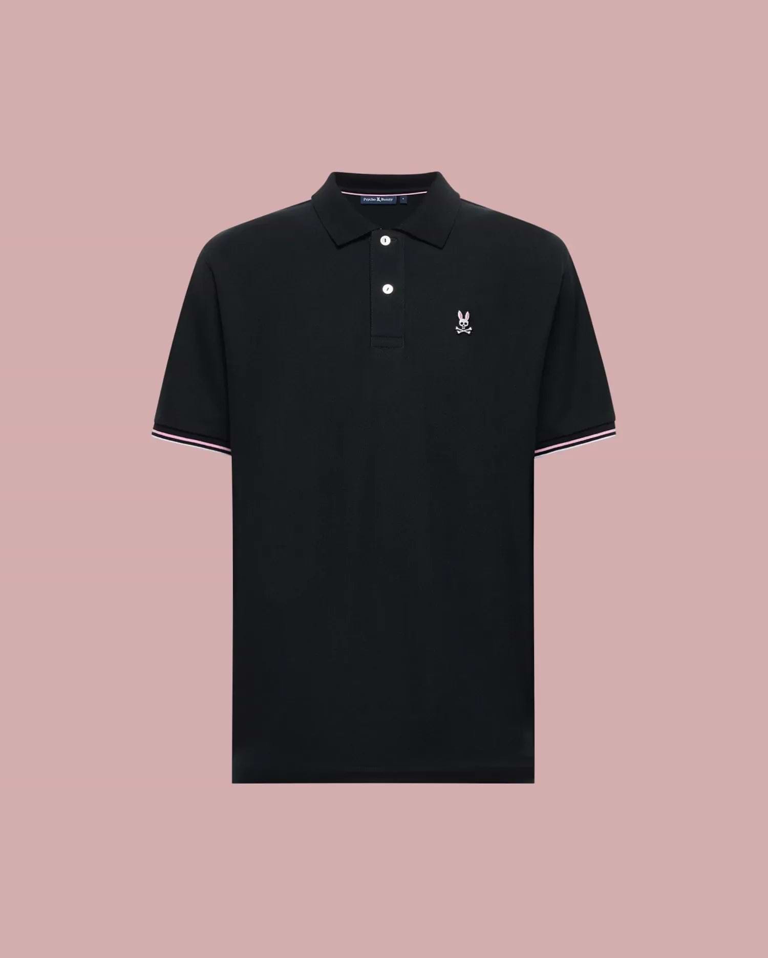 The Psycho Bunny MENS ARCHIVE CLASSIC BUNNY PIQUE POLO (MT0100010) is a black Pima cotton short-sleeve polo with a collar, two buttons, white and pink trim accents, and a white embroidered logo on the chest. Displayed on light pink.