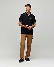 A man stands against a plain background wearing the Psycho Bunny MENS HART PIQUE POLO SHIRT (MT0100032), tan cargo pants, and black shoes. He faces forward, hands relaxed in front of him. (4)